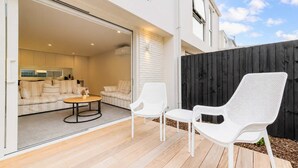 An open patio with a wooden deck, a sofa set, and two white chairs.