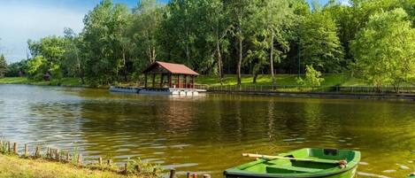 Una escena tranquila junto al lago con un pequeño pabellón de madera y un bote verde.