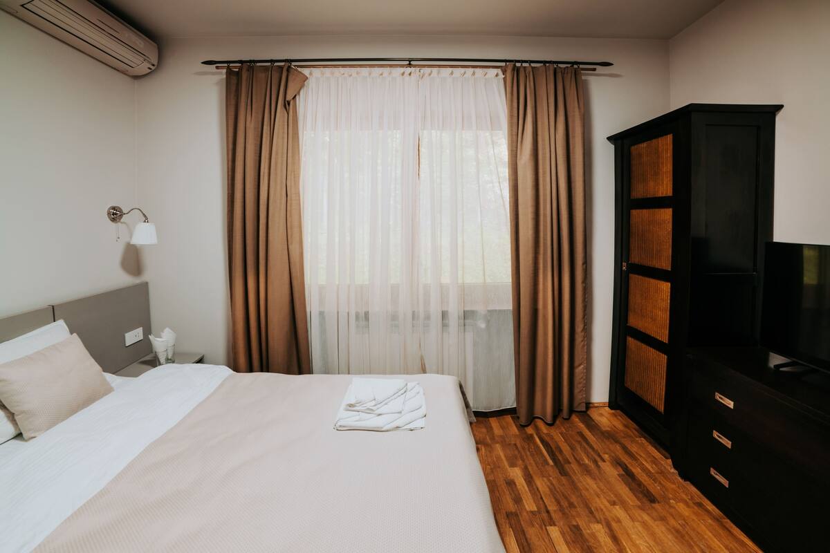 A hotel room with a bed, a wardrobe, a TV, and a window with curtains.