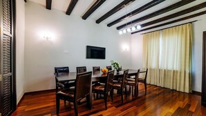 A dining area with a wooden table and chairs, a flat-screen TV mounted on the wall, and a window with curtains. - Lac sub Soare (Iordacheanu)
