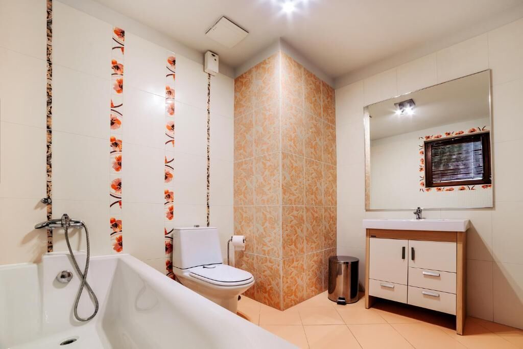 Un baño con bañera, inodoro, tocador con espejo y baldosas estampadas.