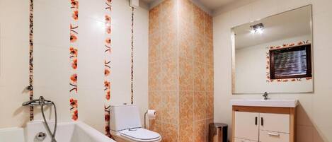 Un baño con bañera, inodoro, tocador con espejo y baldosas estampadas.
