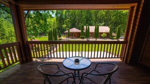 Eine Holzterrasse mit rundem Tisch und zwei Stühlen, mit Blick auf einen gepflegten Rasen und ein Haus mit rotem Dach.