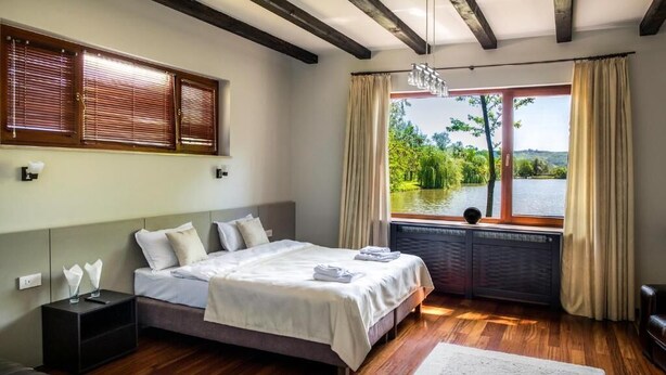 Ein Schlafzimmer mit einem großen Bett, Holzboden, Seeblick und einem Vorhangfenster.