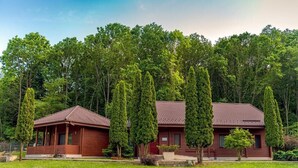 A two-story wooden house with a red-tiled roof, surrounded by a well-maintained lawn and tall trees. - Lac sub Soare (Iordacheanu)