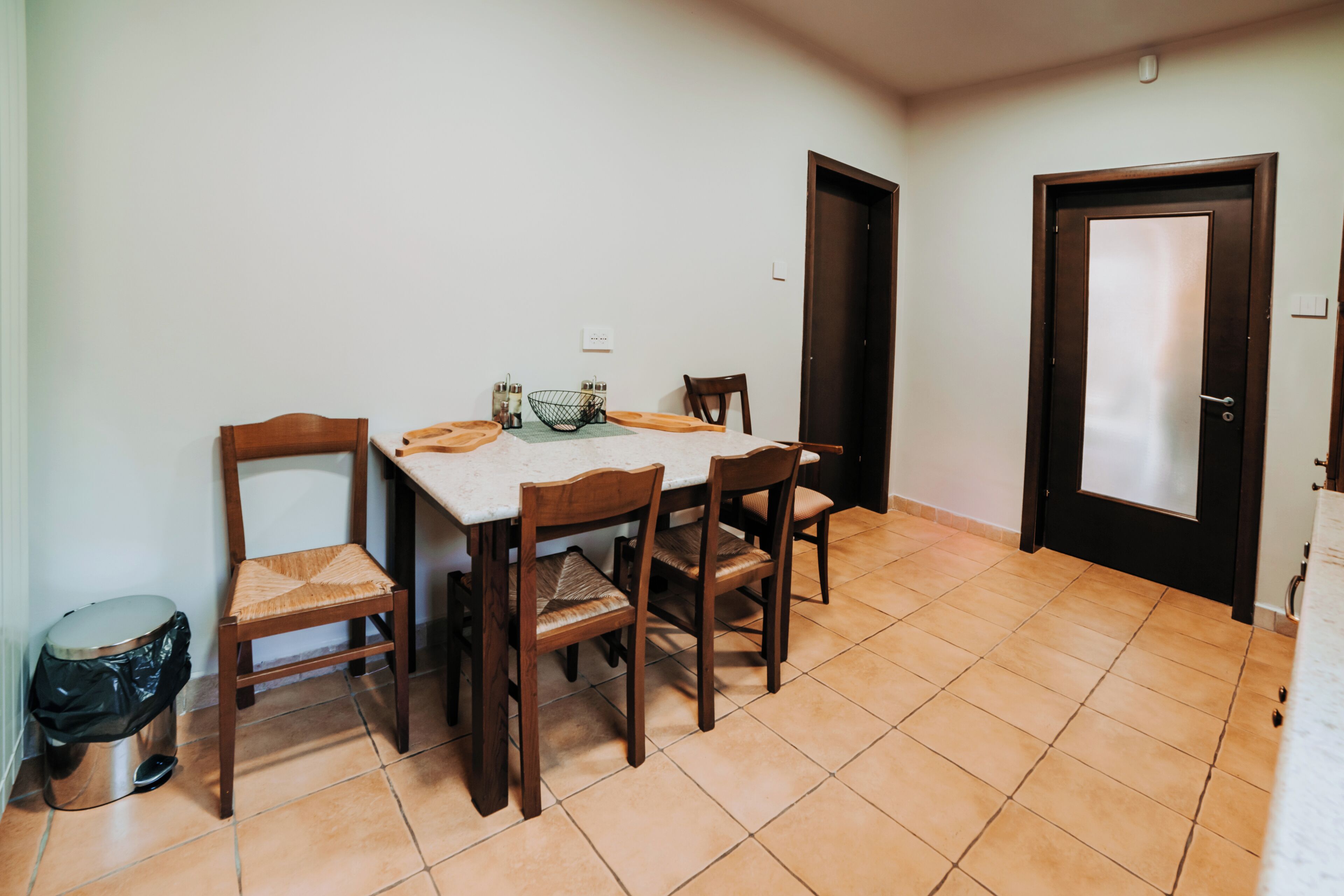 Un comedor con una mesa, cuatro sillas, un cubo de basura y una puerta.