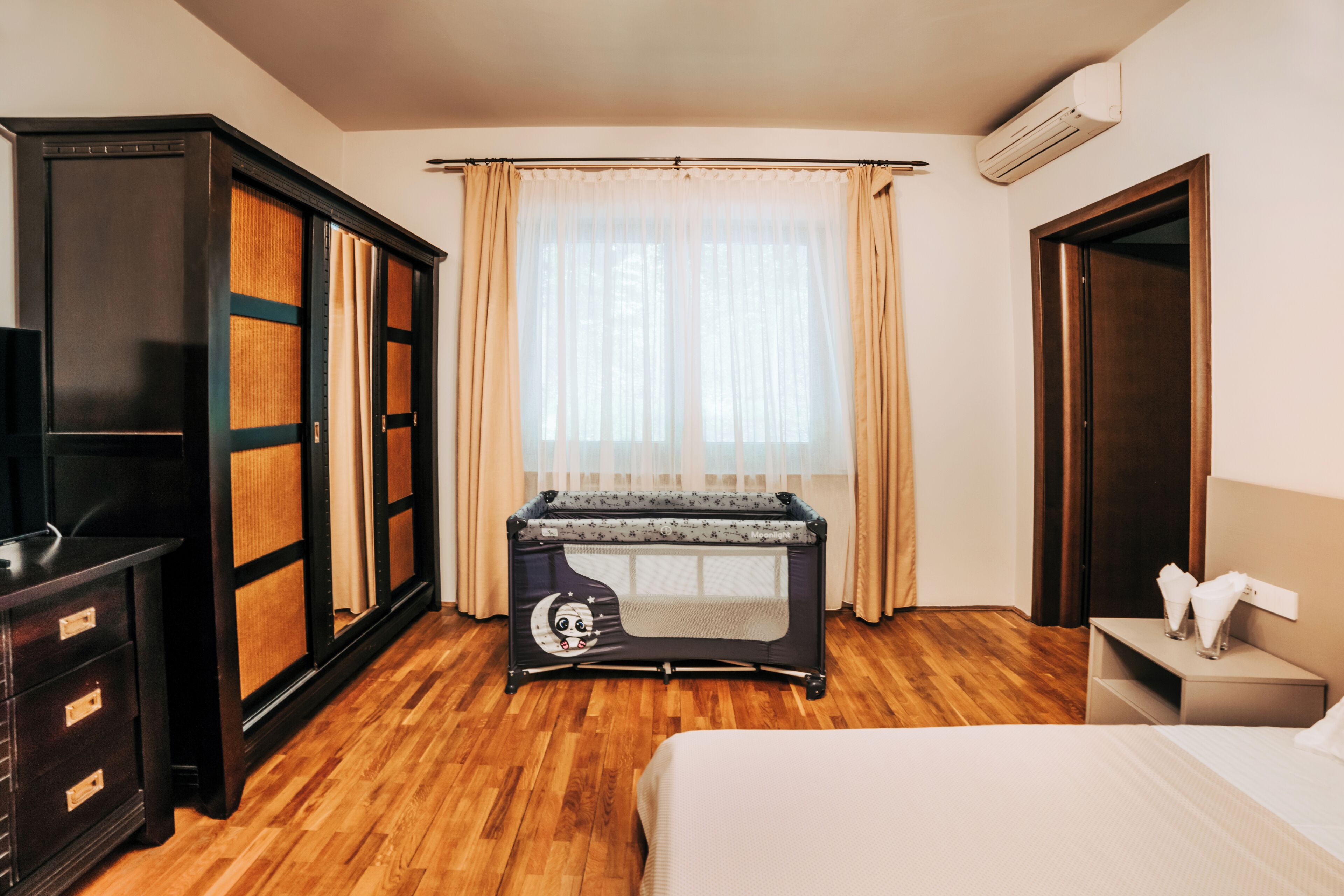 A hotel room with a bed, a desk, a wardrobe, and a window with curtains.