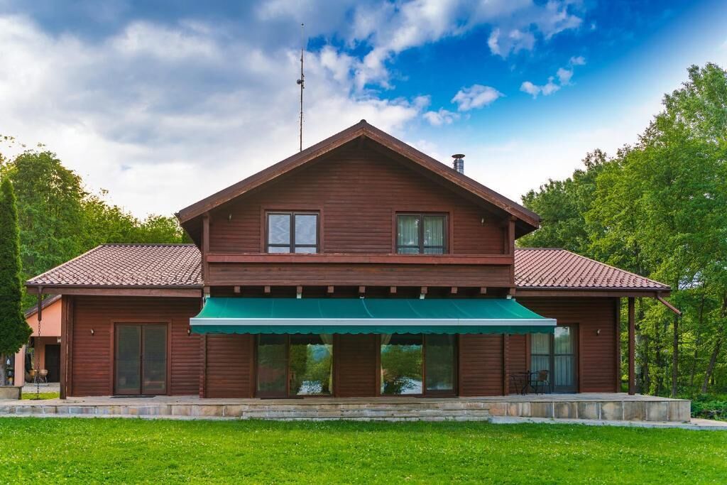 Een houten huis met twee verdiepingen, voorzien van een groen luifel, een pannendak en een schoorsteen.