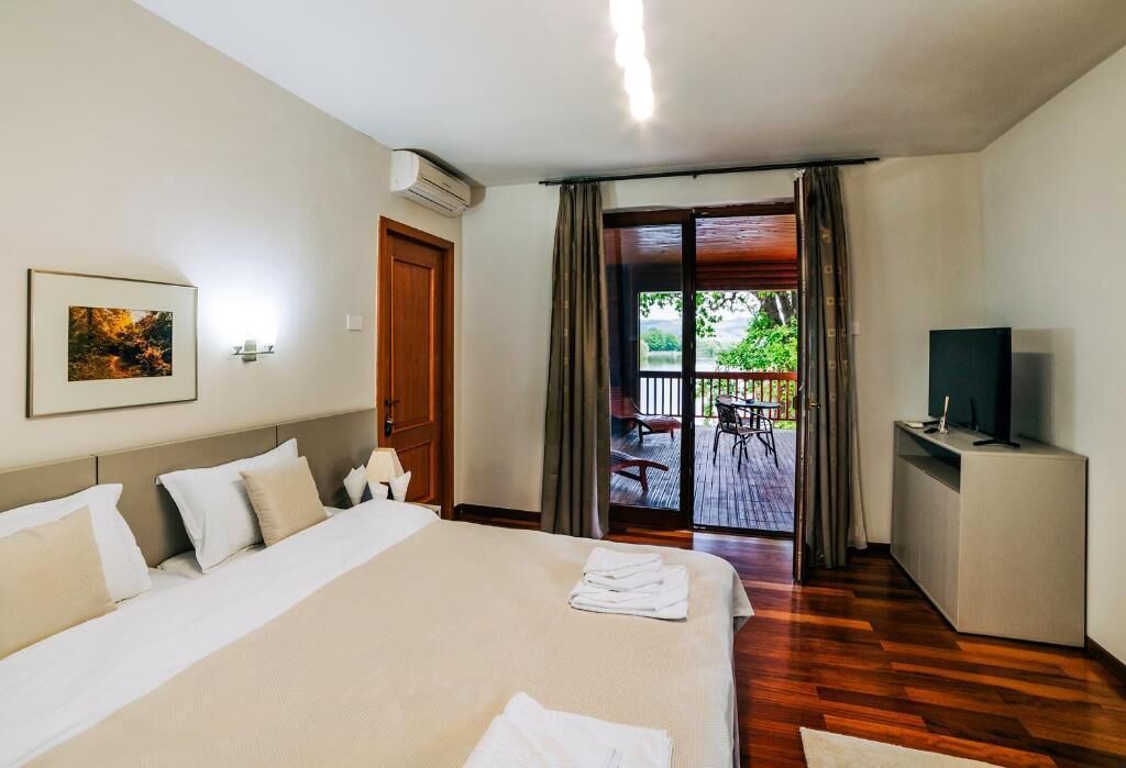 A hotel room with a large bed, a TV, a desk, and a balcony with outdoor furniture.