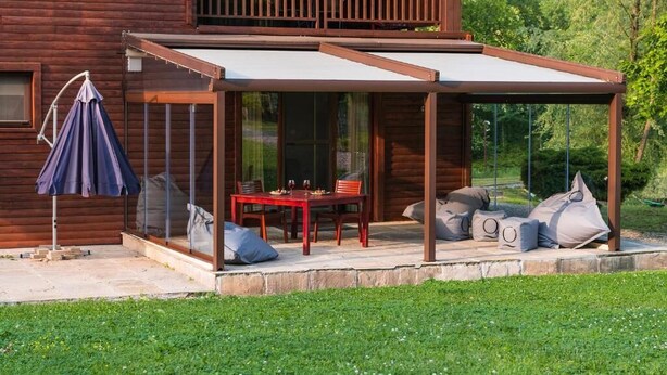 A wooden cabin with a covered patio, a dining table, and outdoor seating. - Lac sub Soare (Iordacheanu)