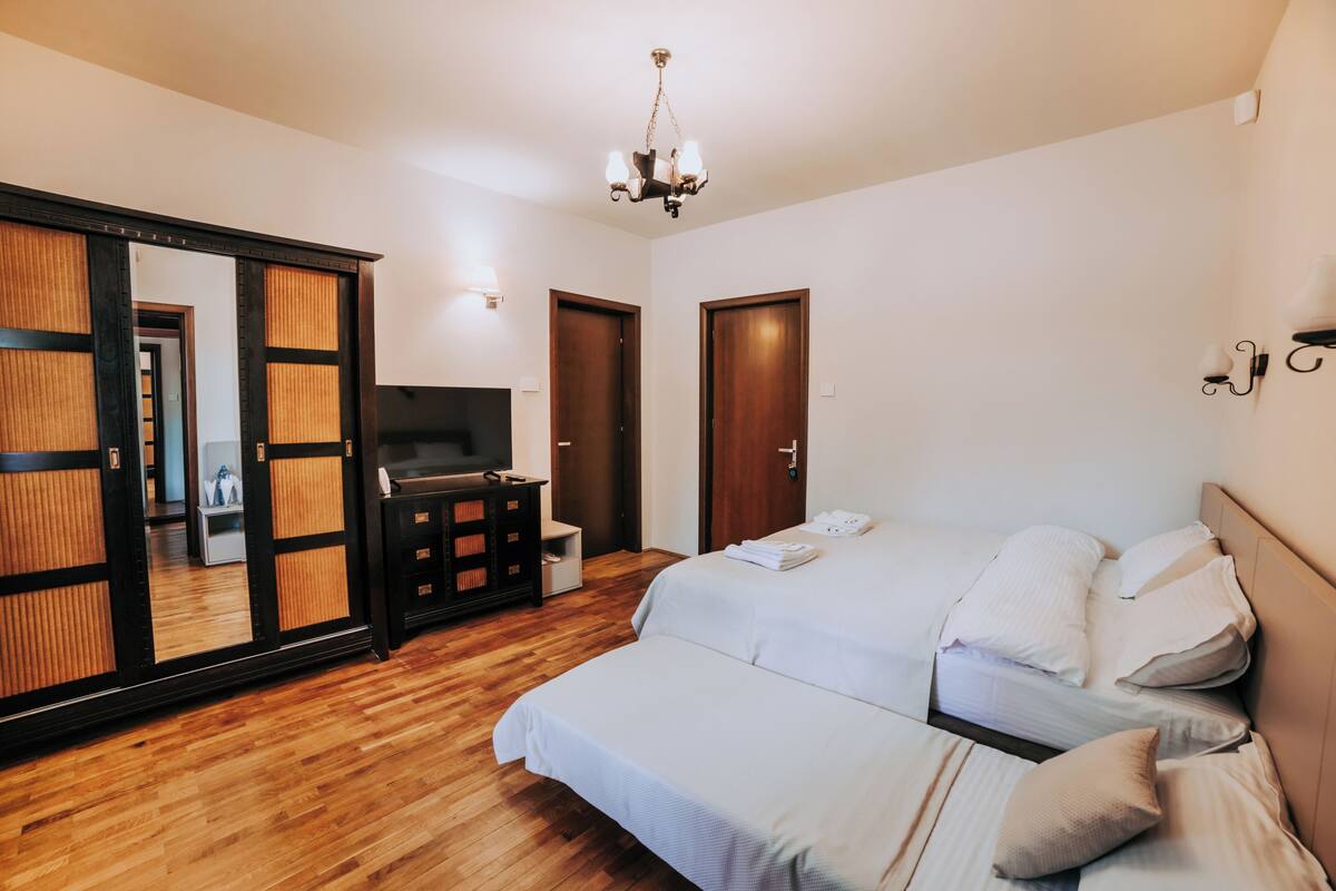 A bedroom with a wooden floor, a bed with white bedding, a TV, a dresser, and a sliding door with a mirror.