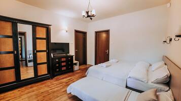 A bedroom with a wooden floor, a bed with white bedding, a TV, a dresser, and a sliding door with a mirror.