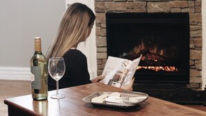 A woman reading a magazine by a fireplace with a bottle of wine and glasses on a table. - Burnima Cottage - situated next to Burnima Homestead at Historic Burnima Estate. (Bombala)