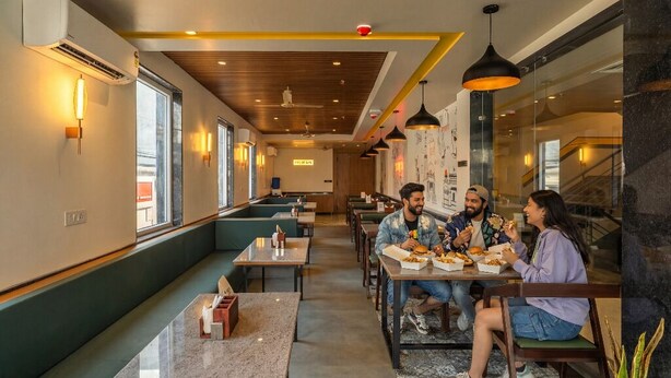 A restaurant with a modern interior, featuring wooden ceiling panels, pendant lighting, and a seating area with tables and benches. - The Hosteller Delhi, International Airport (New Delhi)