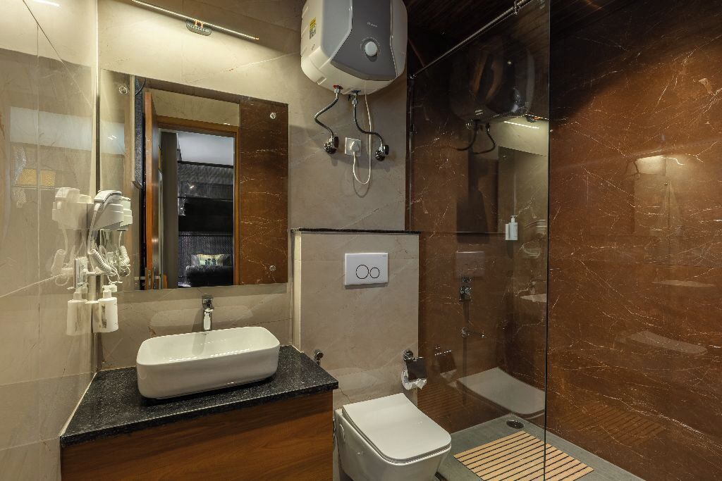 Un baño moderno con un espejo grande, un lavabo sobre encimera, un inodoro y una zona de ducha con mampara de vidrio.