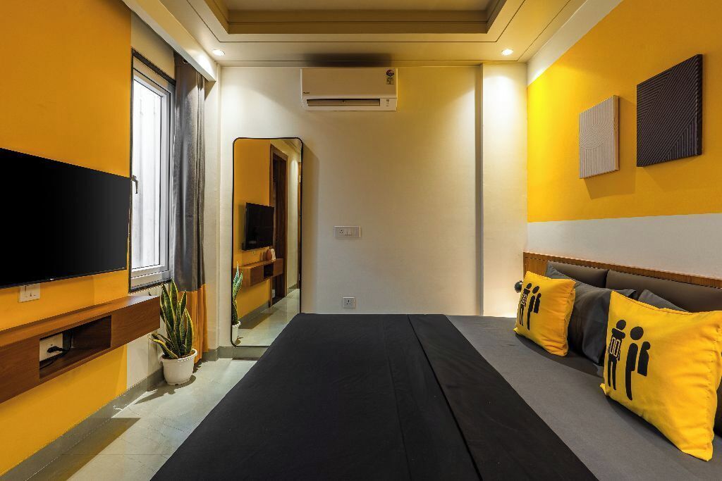 A hotel room with a bed, a TV, a potted plant, and a mirror.