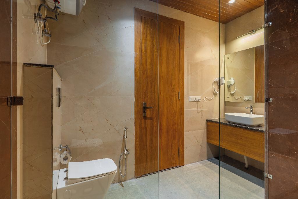 Een moderne badkamer met een houten deur, een glazen douchecabine, een wit toilet en een houten wastafelmeubel met een spiegel.