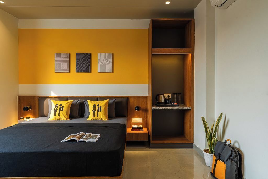 A modern hotel room with a large bed, a nightstand, a wooden shelf, and a potted plant.