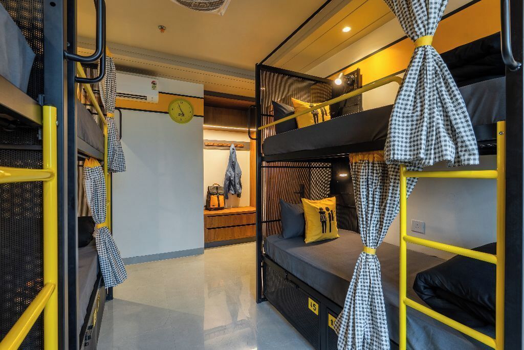 A compact hotel room with bunk beds, a small kitchenette, and a visible clock on the wall.