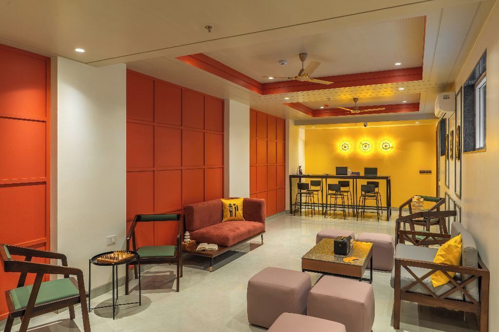 A modern hotel lobby with a red and yellow color scheme, a sofa, chairs, a coffee table, and a dining area with a bar.