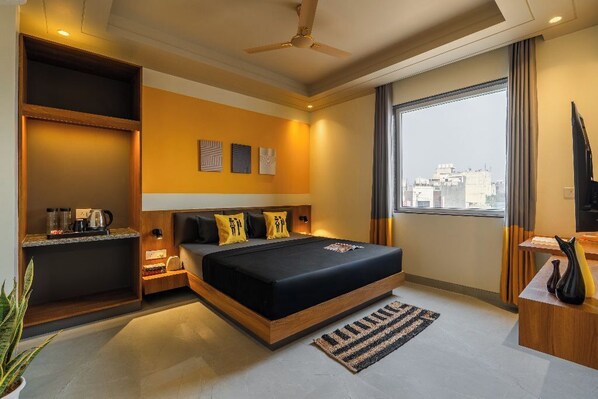A modern hotel room with a large bed, a built-in desk, a large window, and a city view.