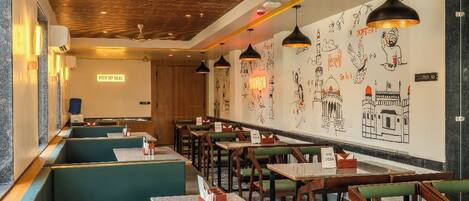 A restaurant with green booths and wooden tables, a wooden ceiling with hanging lights, and walls decorated with black and white drawings.