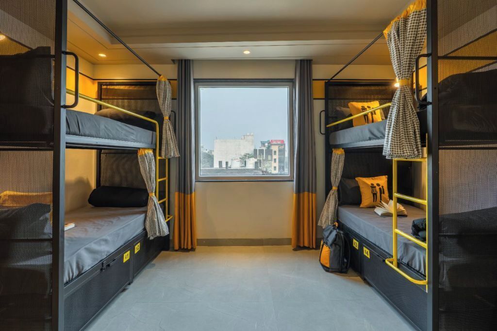 A compact hotel room with two bunk beds, a large window, and curtains.