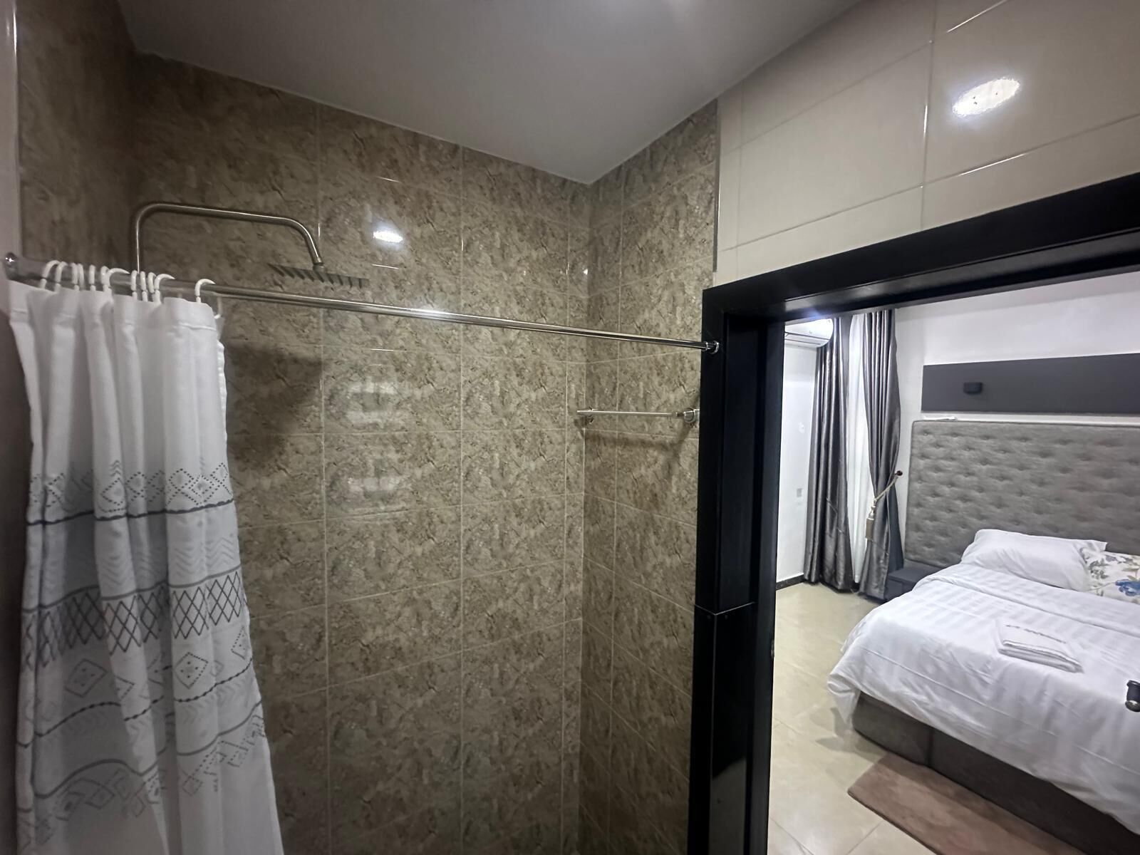 Une salle de bain moderne avec une douche, un porte-serviettes et un lit avec une tête de lit dans la pièce adjacente.