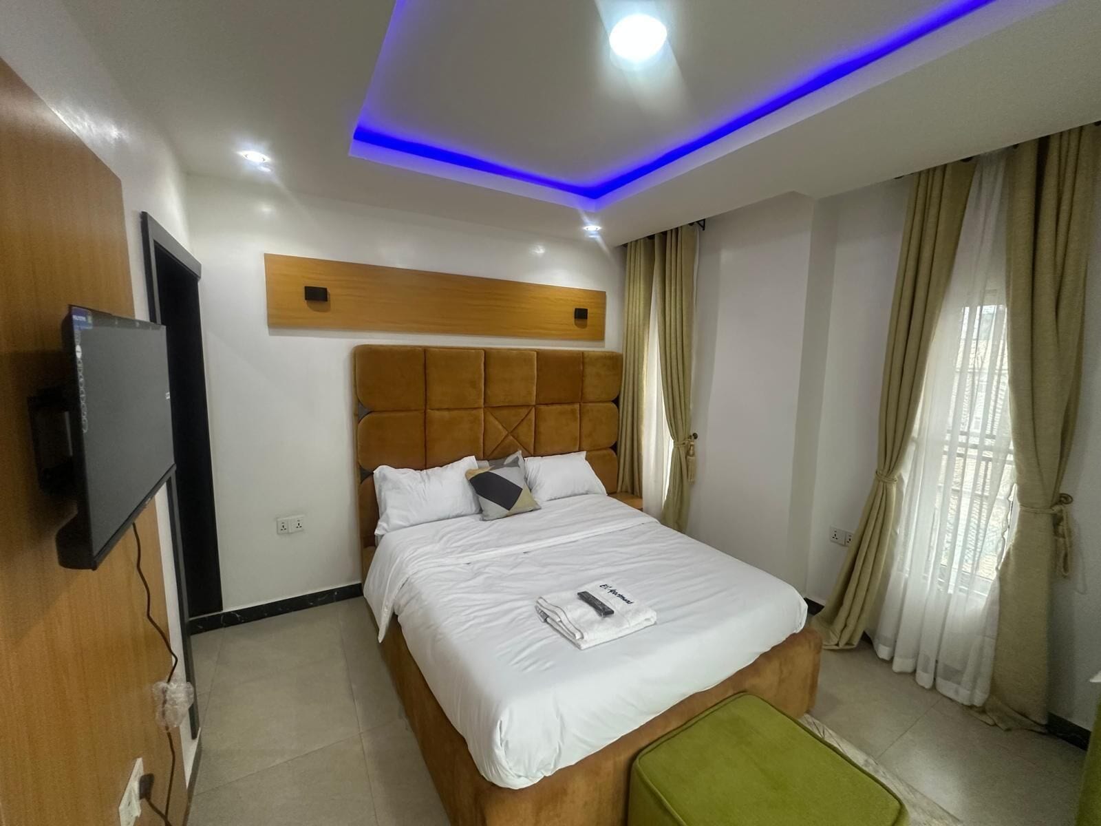 A hotel room with a bed, a TV mounted on the wall, and a ceiling with blue LED lighting.