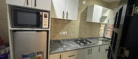 A modern kitchen with white cabinets, a built-in microwave, a refrigerator, a gas stove, and a sink.