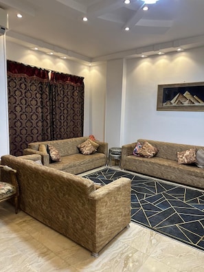 A living room with two sofas, a patterned curtain, a framed picture, and a geometric rug. - Pyramids Gold Sand INN (Giza)