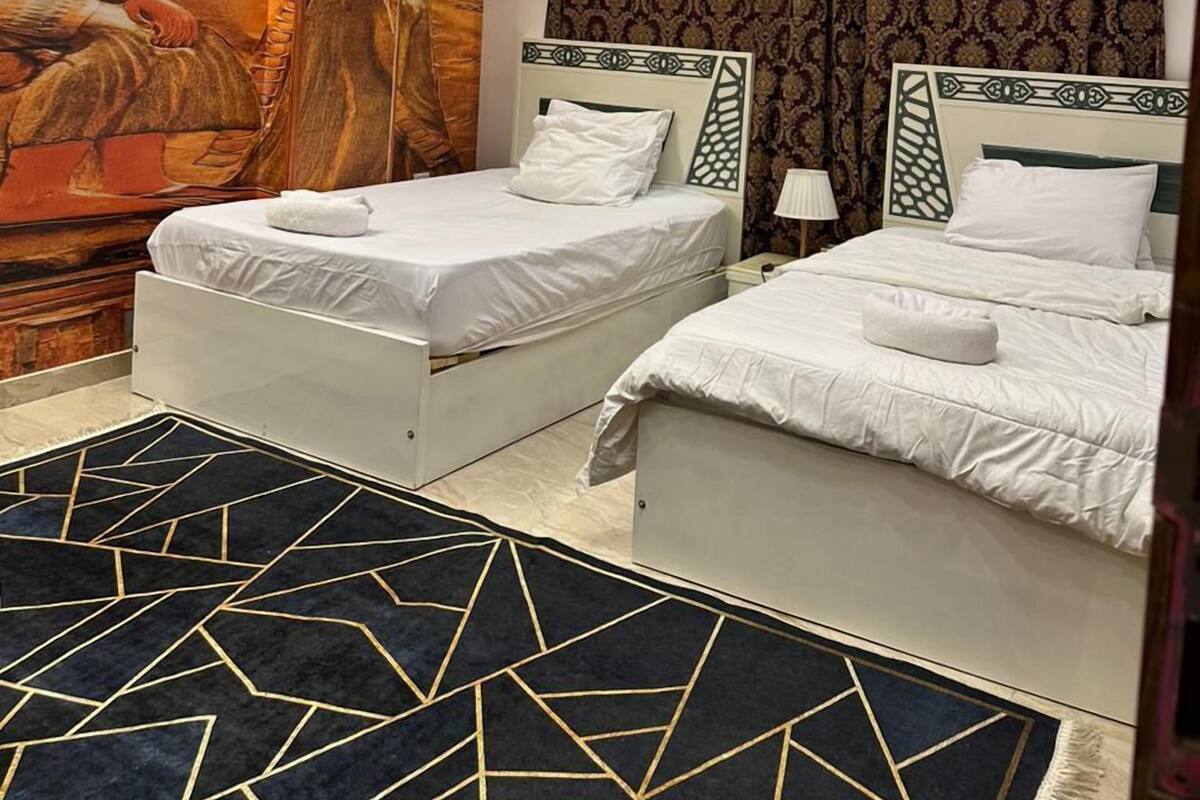 A hotel room with two beds, a large mural, and a patterned carpet.