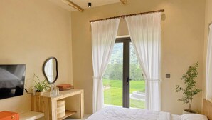 Una camera da letto con un letto, una TV, una scrivania con uno specchio e vista sul verde.