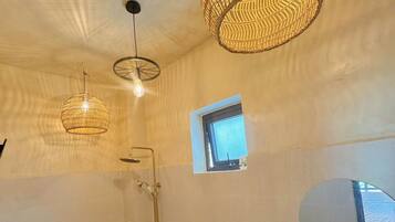 Een badkamer met een toilet, een douche en een wastafel met een stenen wasbak. Er zijn twee hanglampen en een klein raam.