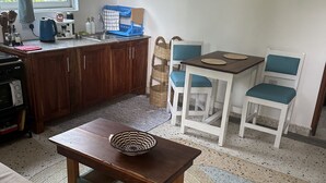 A compact kitchen with wooden cabinets, a dining table with chairs, and a small rug on the floor. - Spacious Deluxe Double Room with AC (Paje)