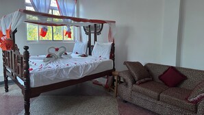 Uma cama de dossel com roupa de cama branca e detalhes vermelhos, um sofá estampado e uma janela com cortinas.