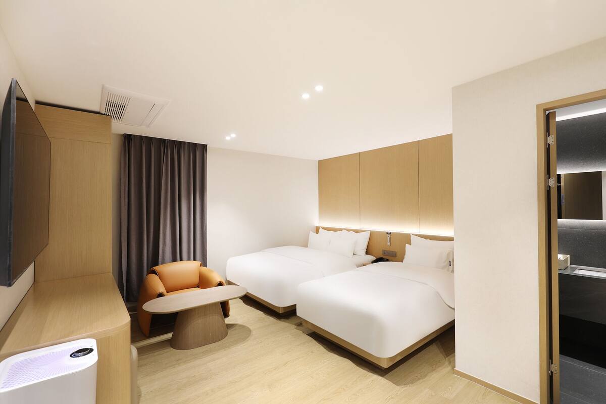 A hotel room with two beds, a small table, a chair, a TV, and a wardrobe.