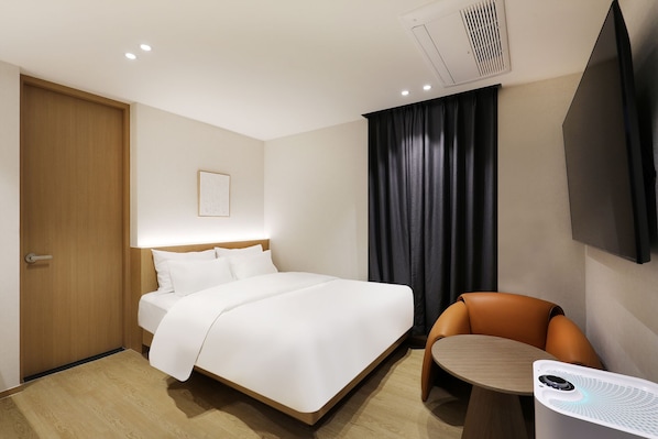 A hotel room with a bed, a chair, a small table, a TV, and a ceiling vent. - Browndot Bucheon (Bucheon)