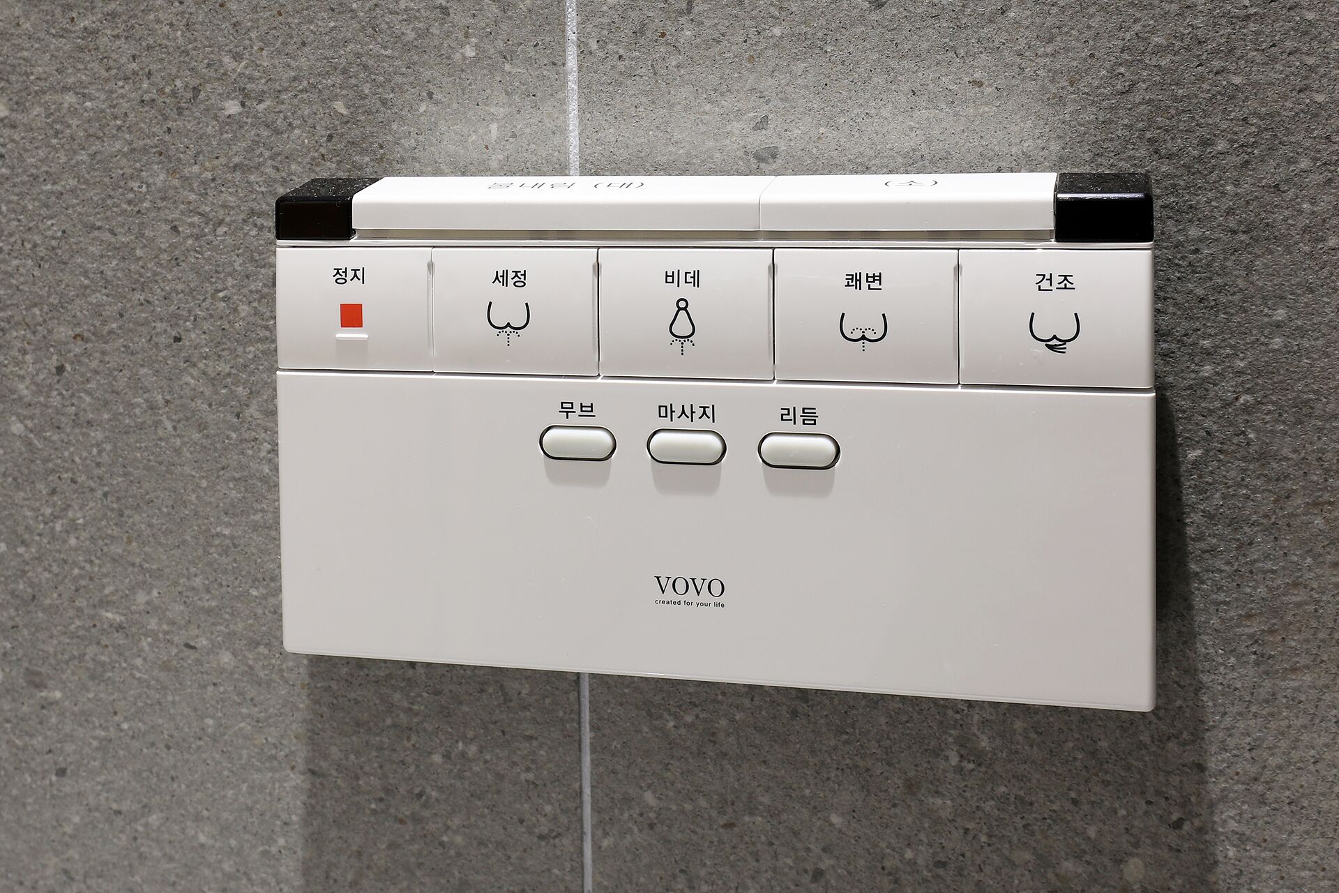 A wall-mounted control panel with various buttons and indicators, including a red light and icons for different functions.