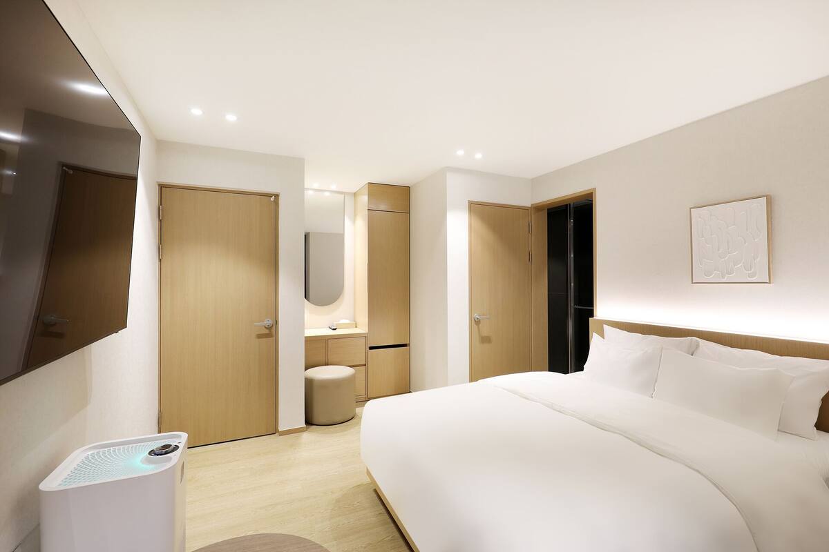 A modern hotel room with a large bed, a bedside table, a mirror, a toilet, and a shower area.