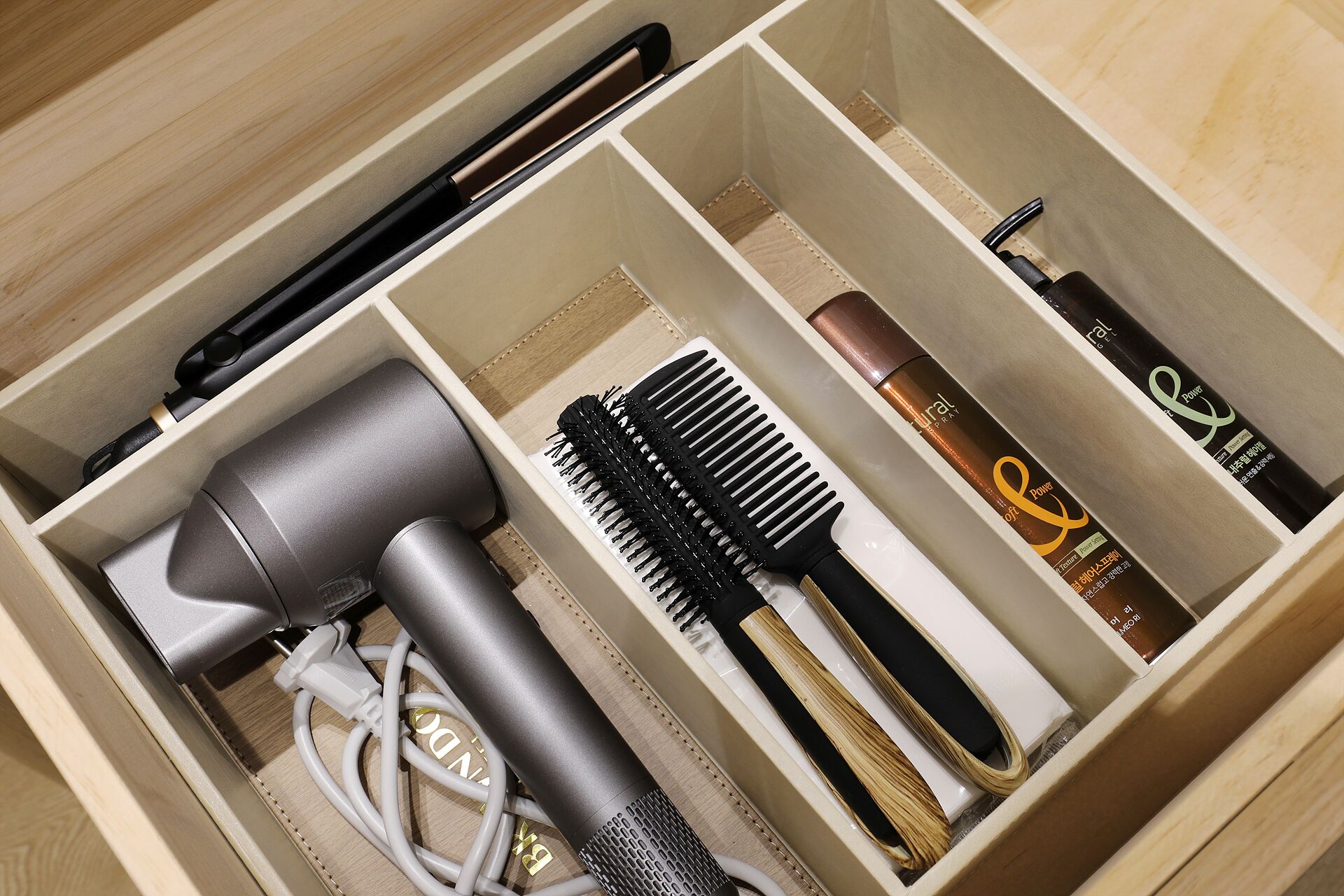 A neatly organized drawer with compartments containing a hairdryer, a comb, a hairbrush, and hair care products.