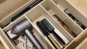 A neatly organized drawer with compartments containing a hairdryer, a comb, a hairbrush, and hair care products.