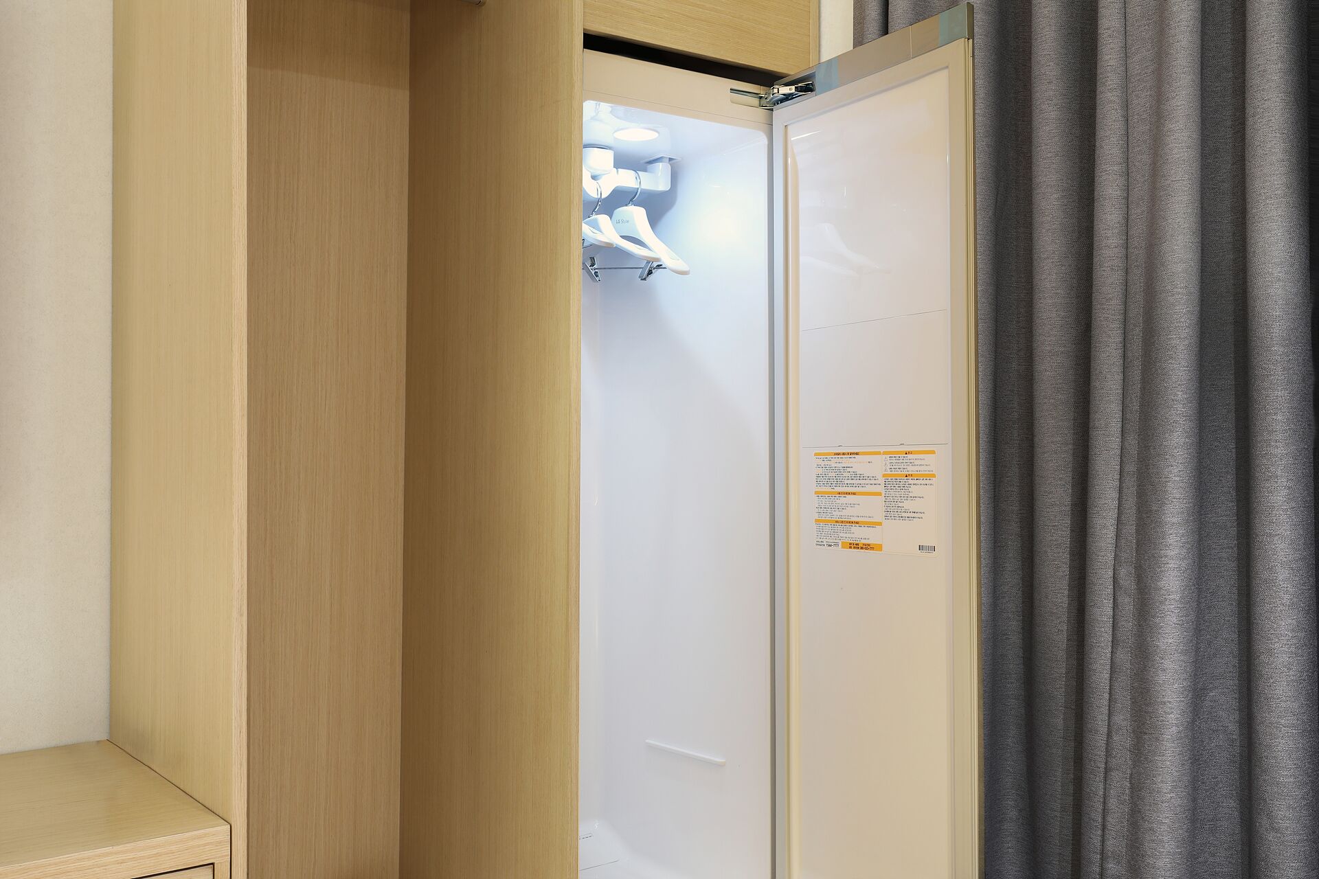 A hotel room with a wooden wardrobe, a white door with a label, and grey curtains.