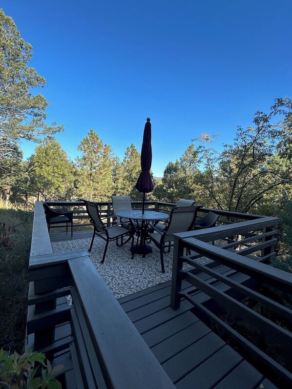 Eine Terrasse im Freien mit einem runden Tisch, Stühlen und einem großen Sonnenschirm.