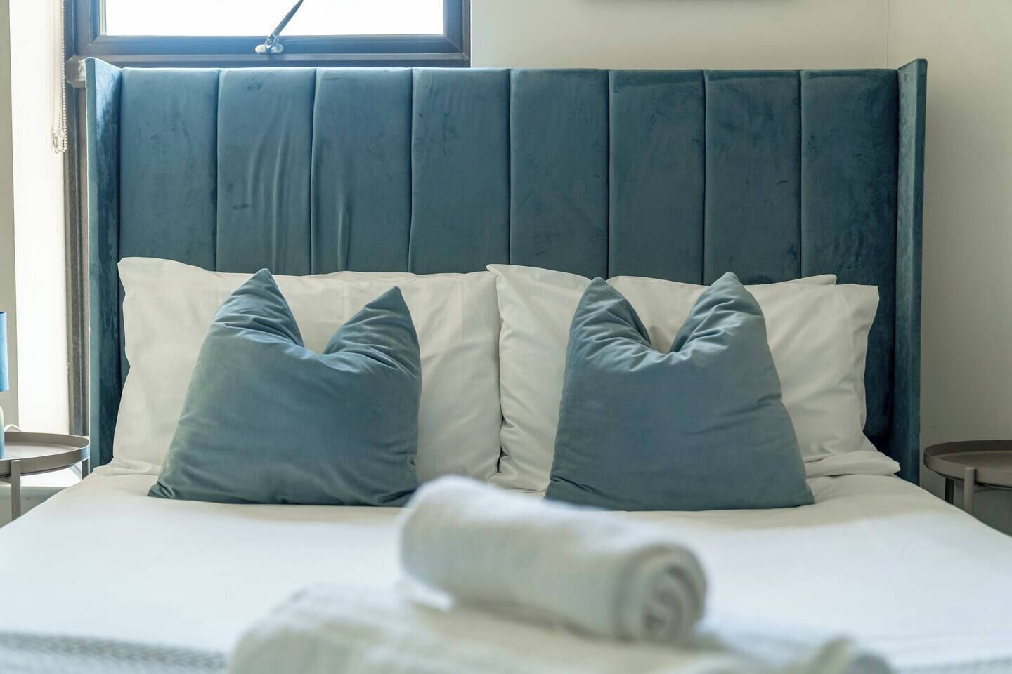 Una cama con cabecera, dos almohadas y una toalla enrollada.