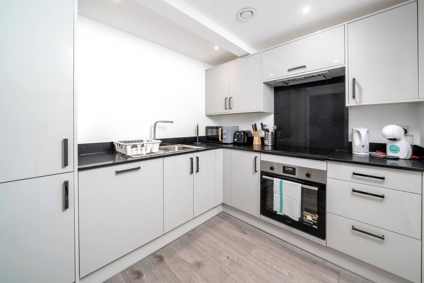 A modern kitchen with white cabinets, a black countertop, and stainless steel appliances.