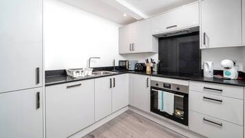 A modern kitchen with white cabinets, a black countertop, and stainless steel appliances.