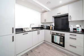 A modern kitchen with white cabinets, a black countertop, and stainless steel appliances. - Chic 1-Bed Apartment in Ealing (London)