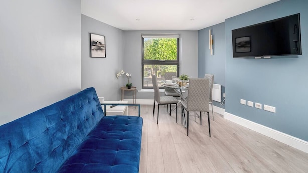 Ein modernes Wohnzimmer mit einem blauen Sofa, einem Esstisch, Stühlen und einem an der Wand befestigten Fernseher.