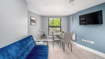 A modern living room with a blue sofa, dining table, chairs, and a TV mounted on the wall.